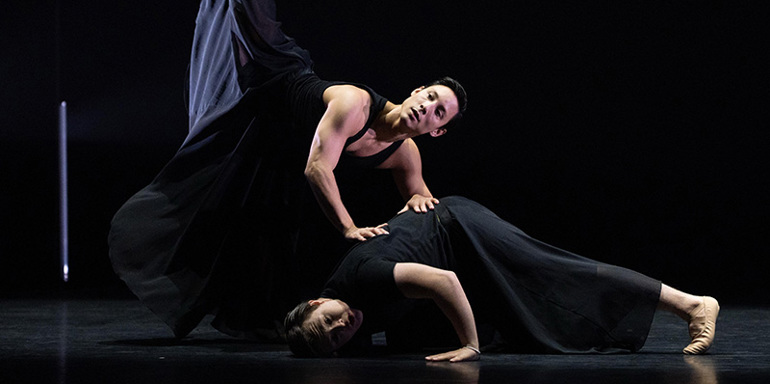 Two male ballet dancers together on stage in black clothing