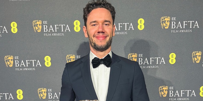 Marcin Mazurek at 2025 BAFTAs, in front of BAFTA backdrop and holding award