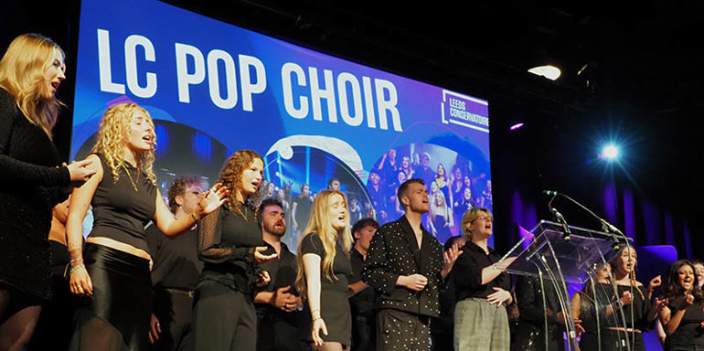 LC Pop Choir performing on stage with large LC Pop Choir graphic on screen behind them